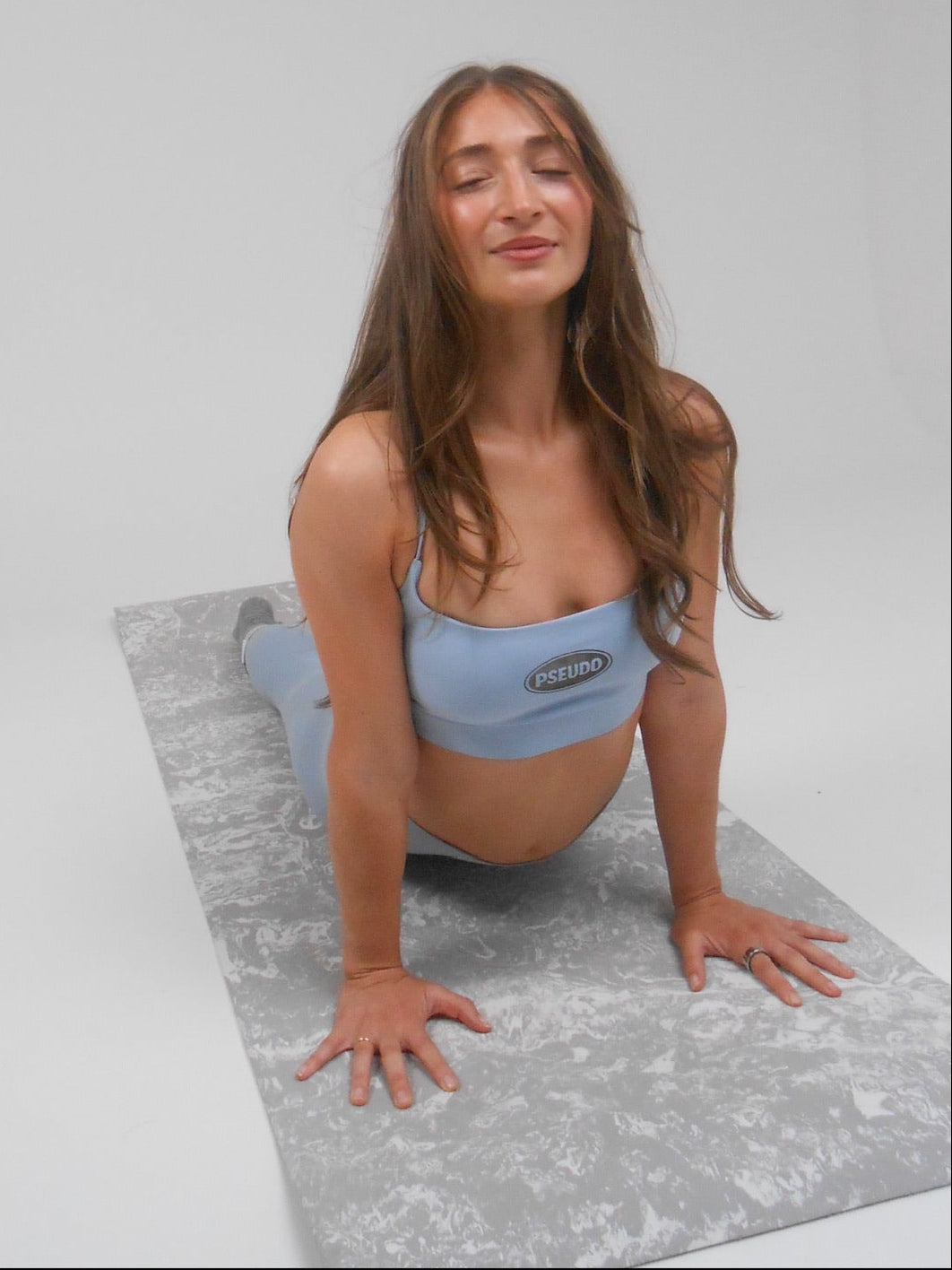 Woman in a yoga pose on a gray mat with a plain background